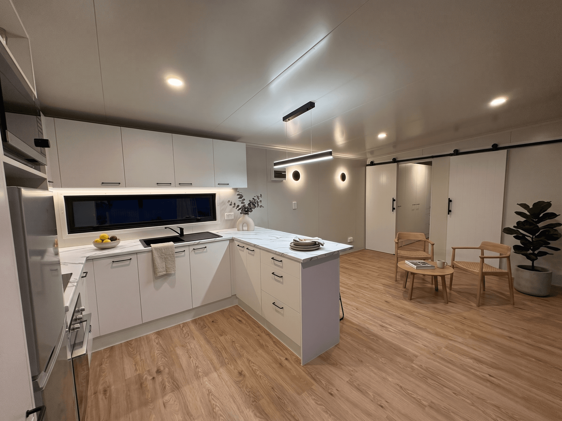 Open-plan kitchen and living area with marble benchtop, timber chairs and sliding barn doors