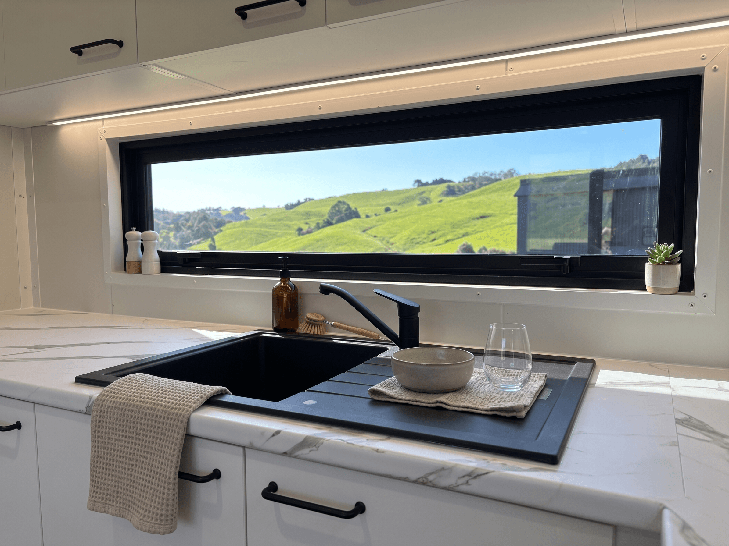 Finished economy home kitchen with black granite sink and picture window overlooking NZ hills