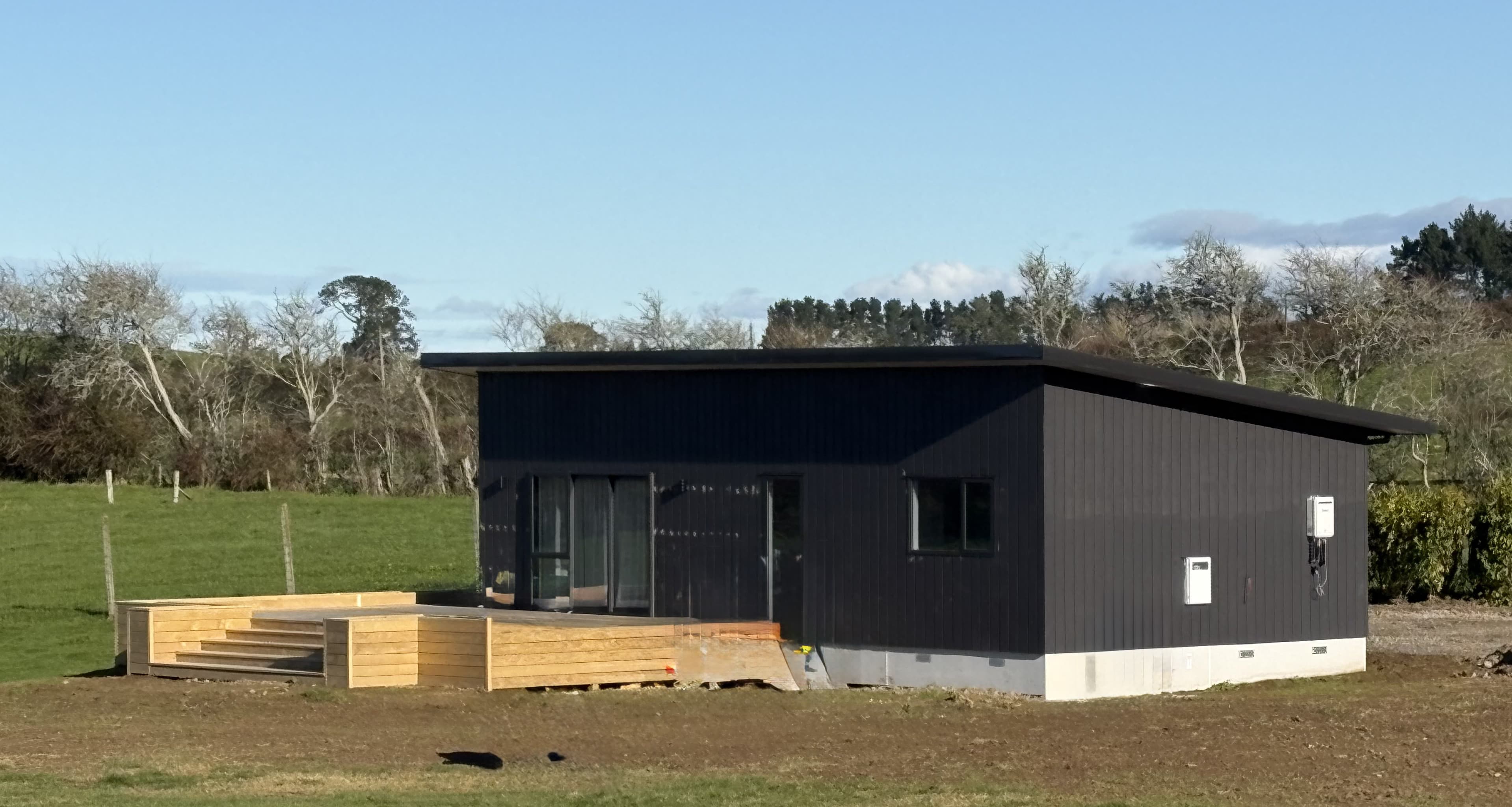 Black NZ-made transportable family home with timber deck on a Te Kōwhai rural section